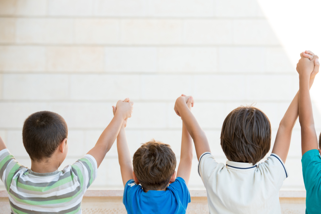 Un groupe d'enfant se tenant debout de dos avec les bras en l'air en se tenant tous les mains, pour symboliser l'union.