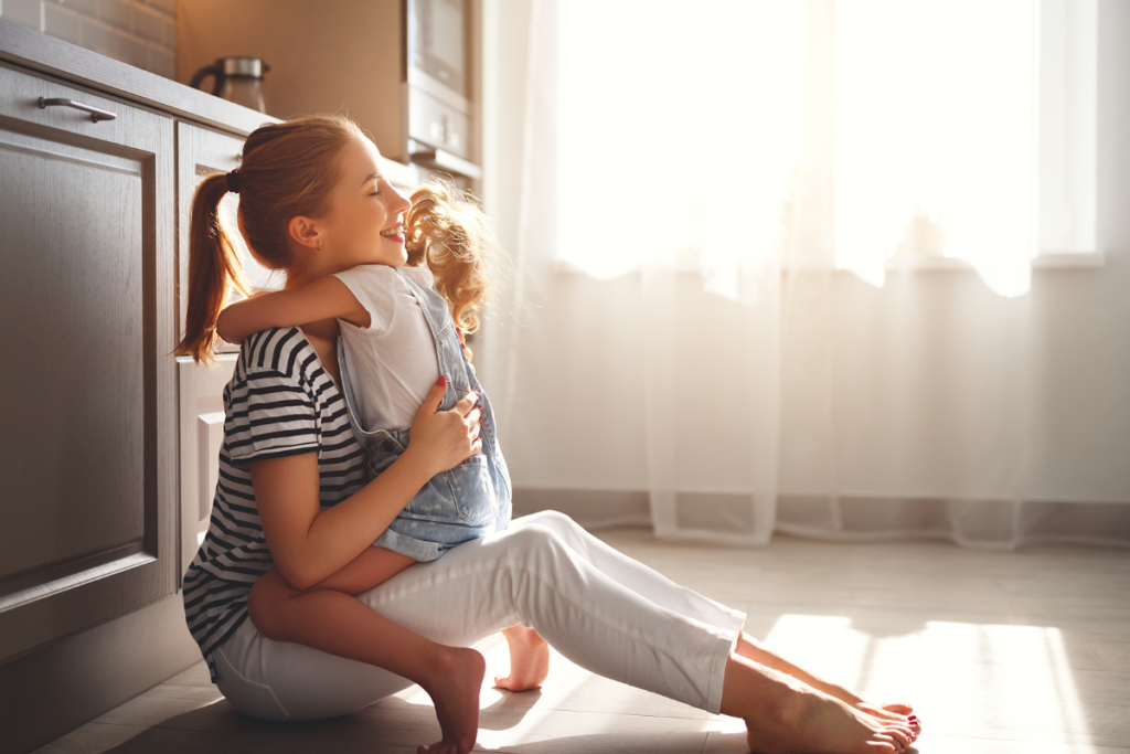 Une maman faisait un câlin à sa fille assise au sol de sa cuisine.