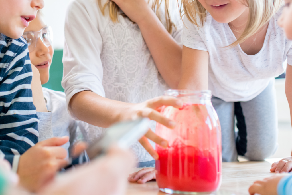 Des enfants qui réalisent l'expérience du volcan dans un bocal avec du colorant alimentaire rouge.